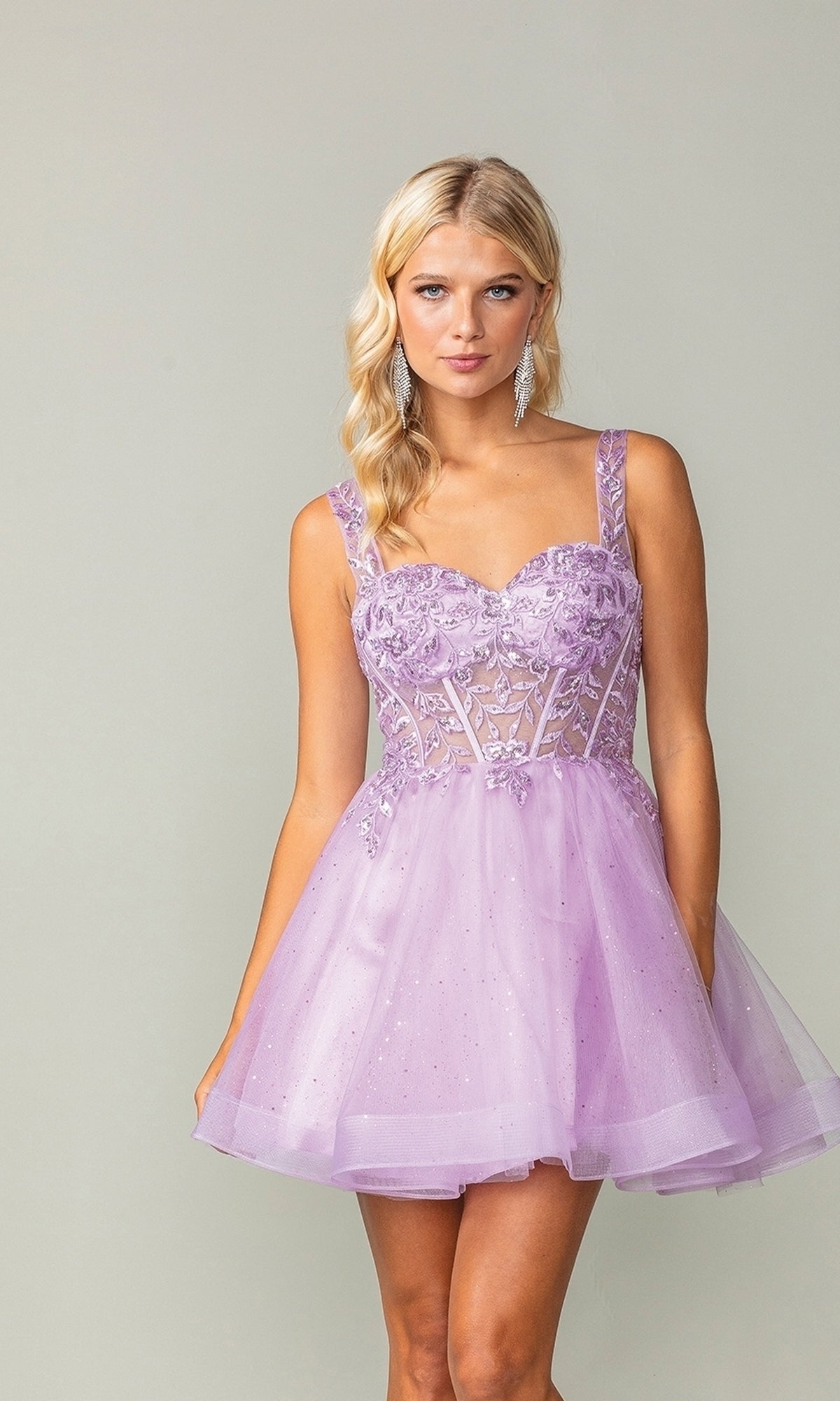 A woman wears the Embroidered-Bodice Short Lace-Up Hoco Dress 3390, a lilac floral corset babydoll dress with a sheer bodice, standing against a plain light gray background.